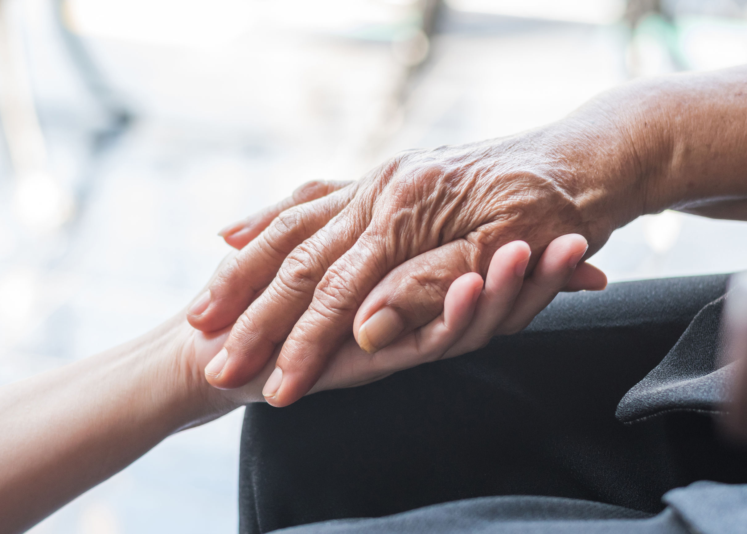 Senior in wheelchair, hand held by caregiver