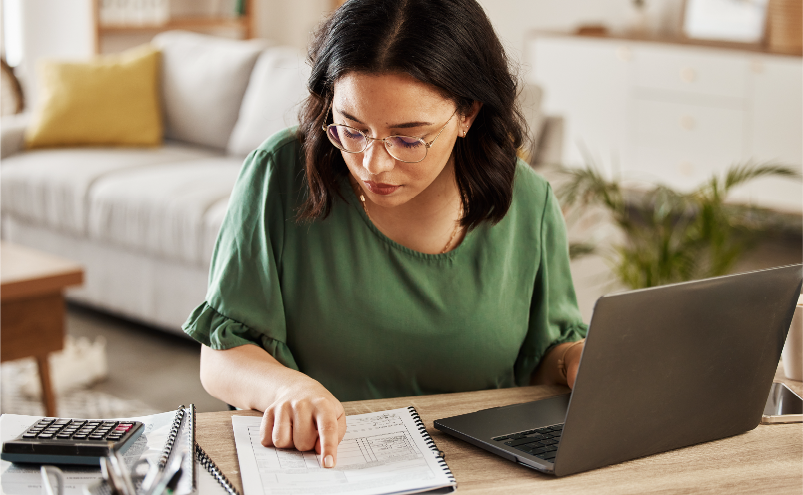 woman using a laptop and financial paper to file taxes in her home